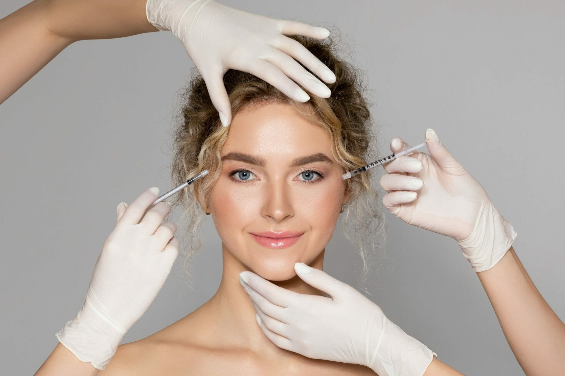 Attractive young woman getting injection for eyes area by two cosmetologists giving anti aging serum