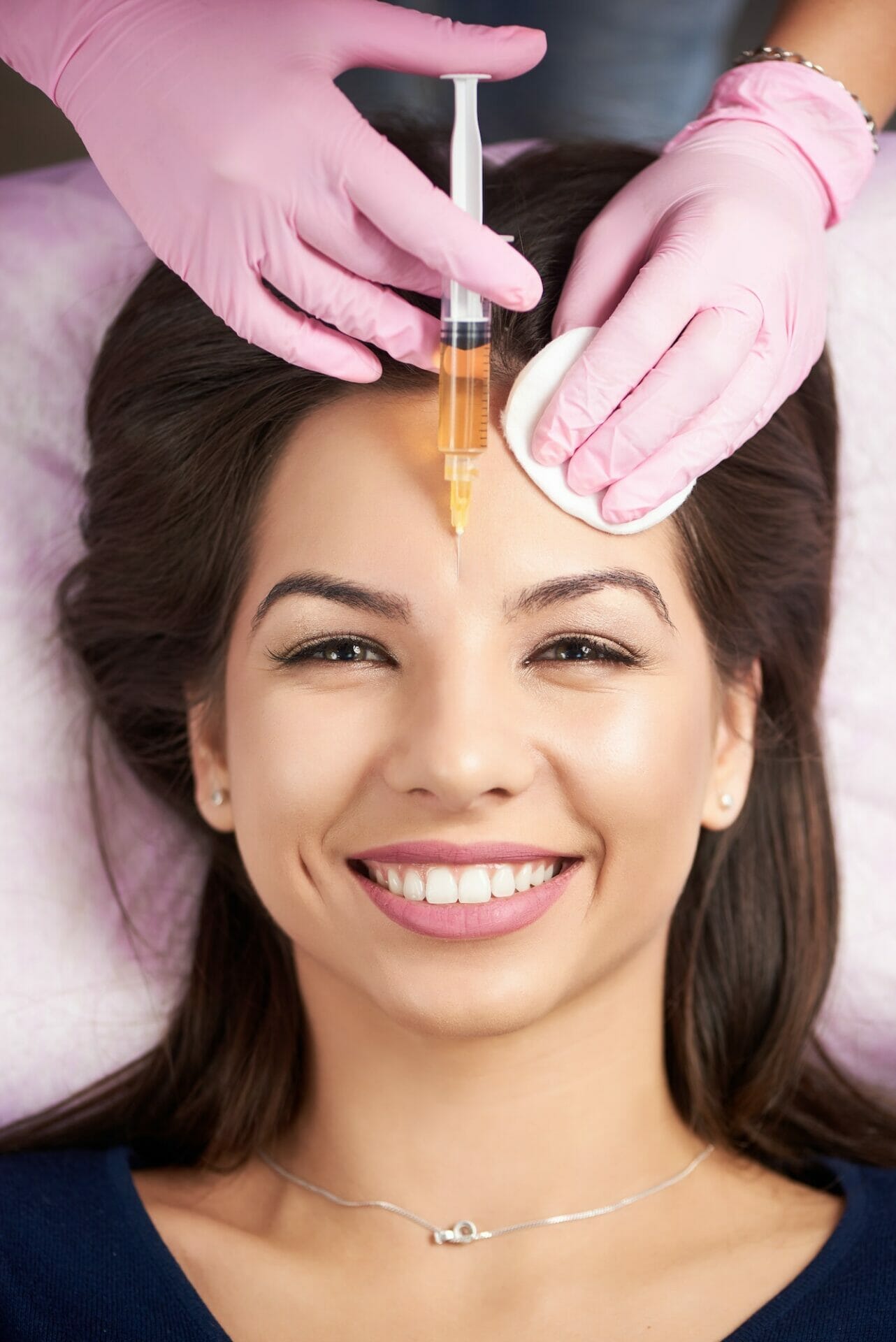 Smiling woman getting injection for female forehead face in the cosmetology salon.